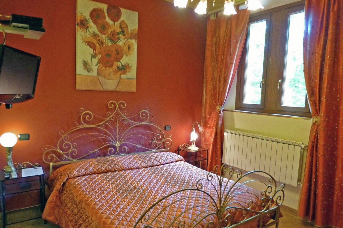 Une chambre à coucher avec un lit en métal, une table de chevet avec une lampe, un radiateur et une fenêtre avec des rideaux.
