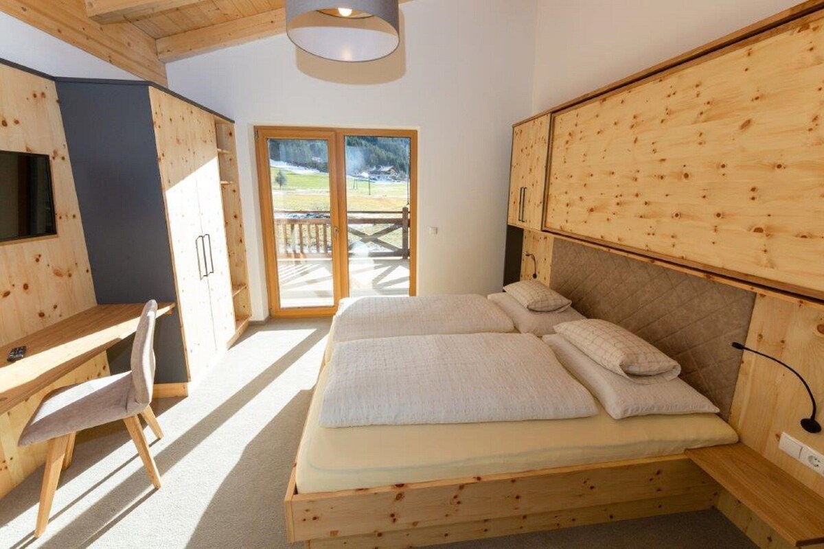 A wooden bedroom with a bed, a desk, and a chair.