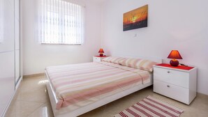 A bedroom with a bed, two bedside tables, a nightstand, a window with blinds, and a wall-mounted painting. - Tasteful Apartment in Medulin With Private Balcony (Medulin)