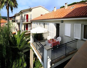 A balcony with a table and chairs, a white umbrella, and a view of neighboring buildings. - Apartment in San Bartolomeo Al Mare (San Bartolomeo al Mare)
