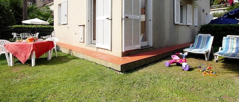 A small house with a patio, white shutters, and a table with a red tablecloth.