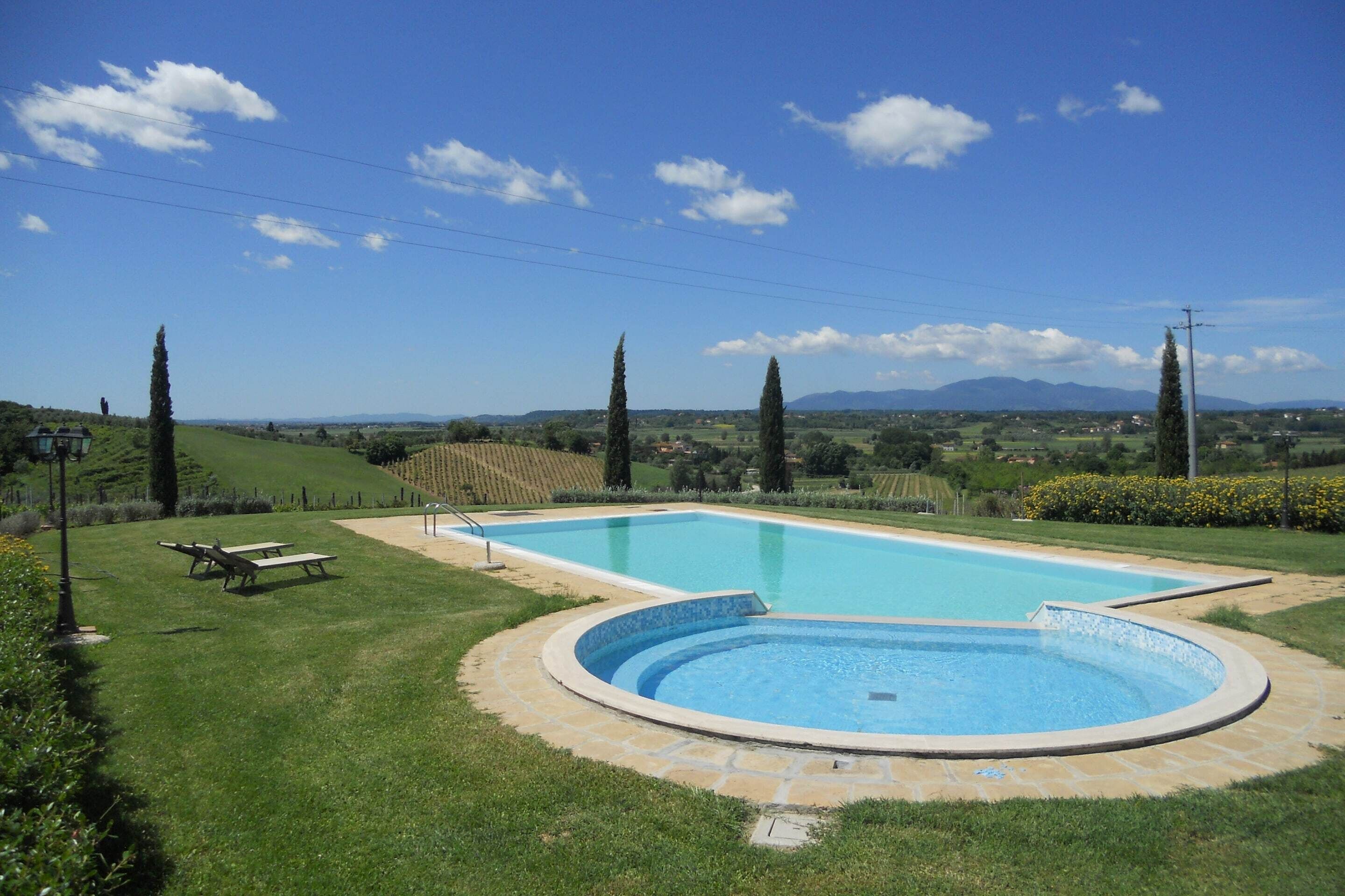Une piscine bordée de pierres, entourée d’une pelouse et agrémentée de deux tables de pique-nique.