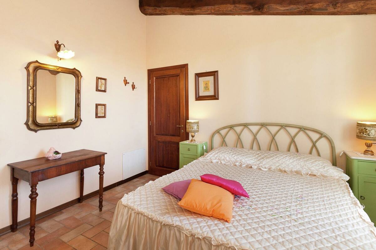Een slaapkamer met een bed, een houten dressoir, een spiegel en een deur.