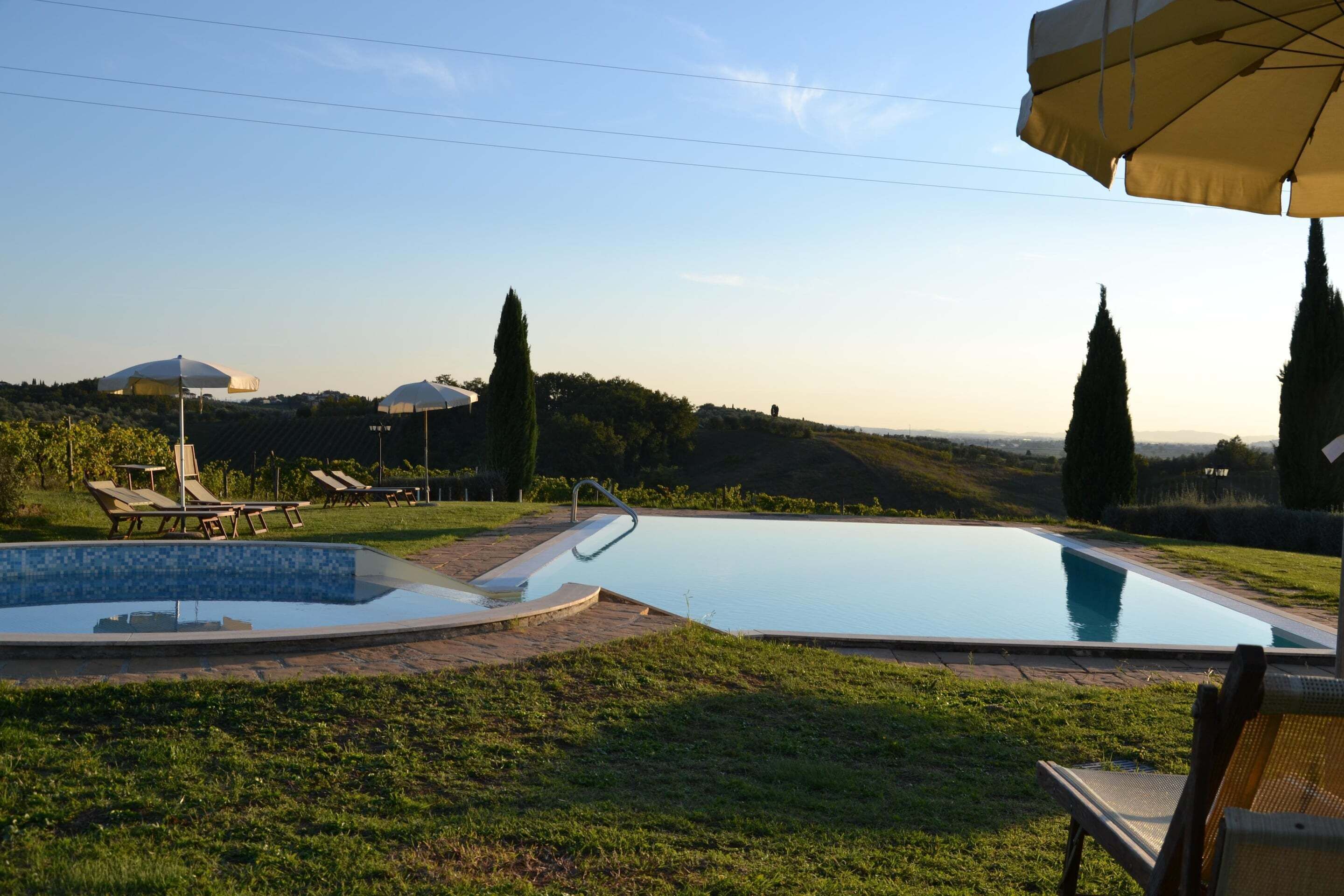 A swimming pool with lounge chairs and umbrellas, surrounded by grass and trees.
