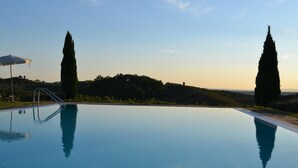 Une piscine paisible aux eaux d’un bleu limpide, entourée d’un jardin aménagé et de grands cyprès.