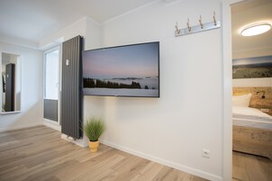 Una sala moderna con un televisor de pantalla plana grande montado en la pared, una planta en maceta y una cama con cabecera de madera.