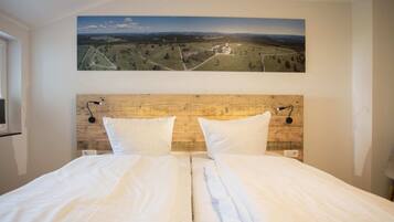 A double bed with a wooden headboard, two bedside lamps, and a landscape painting above.