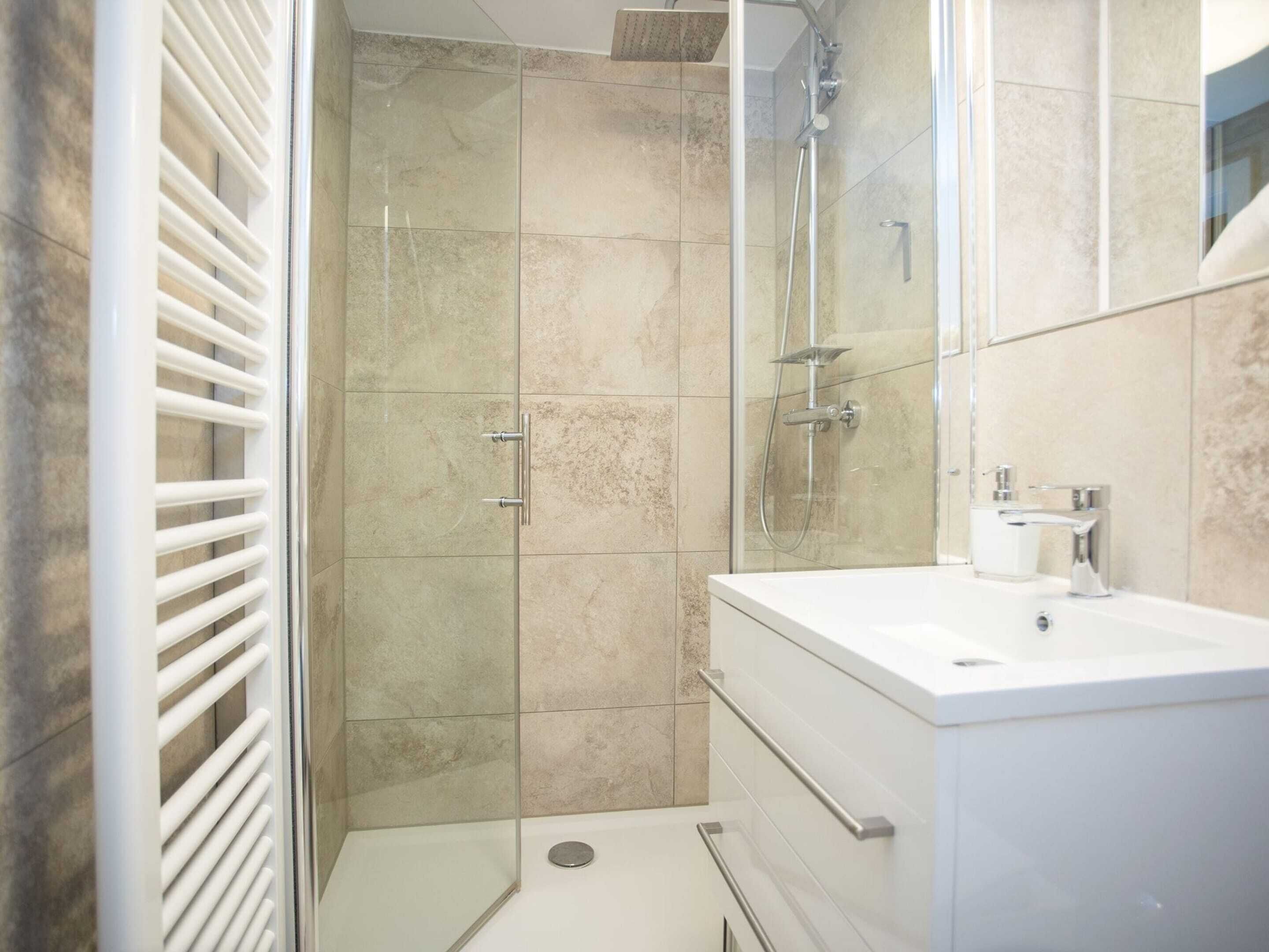A modern bathroom with a glass-enclosed shower, a white sink, and a mirror.