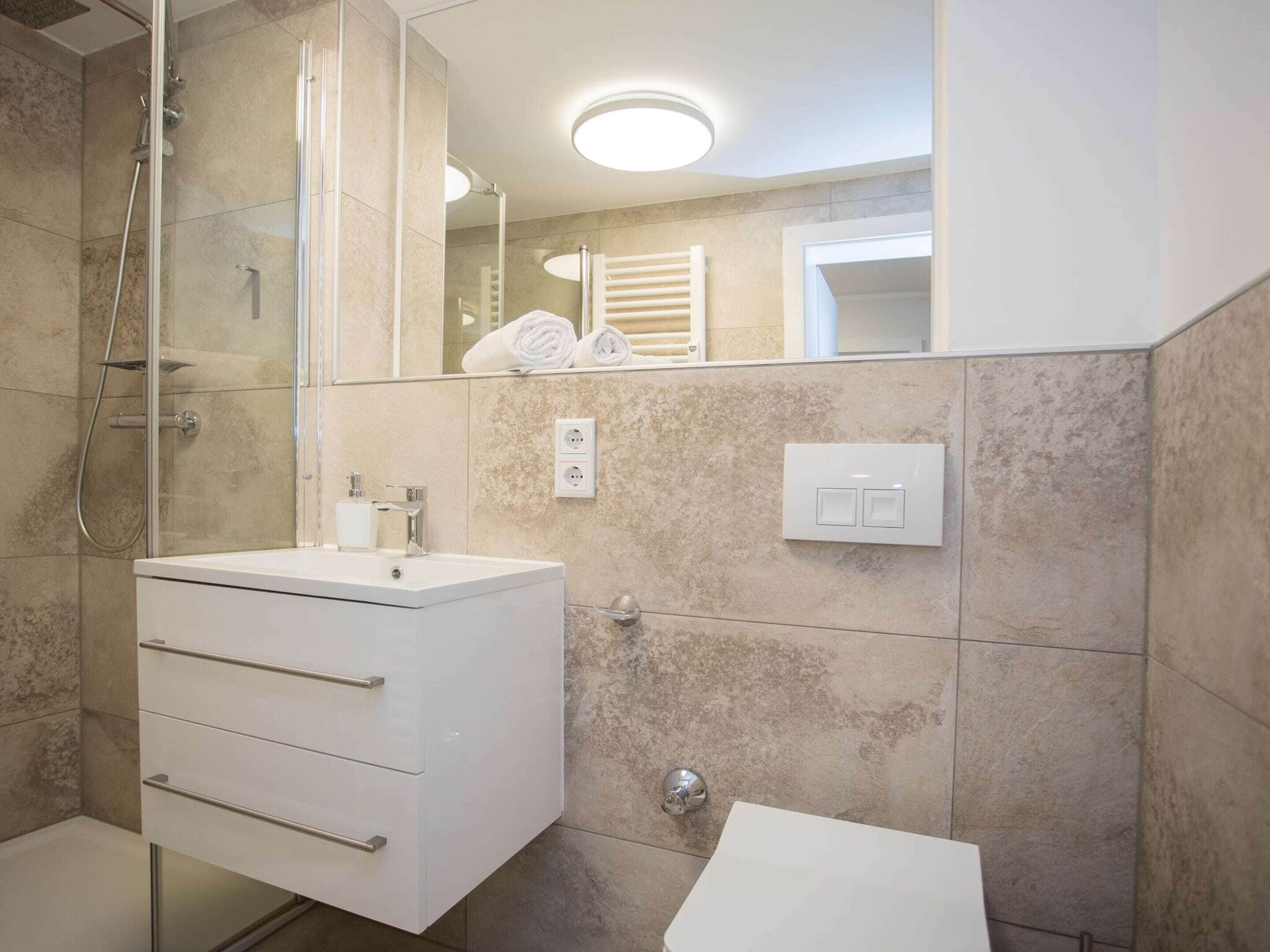 A modern bathroom with a glass-enclosed shower, a white vanity with drawers, a mirror, and a towel rack.