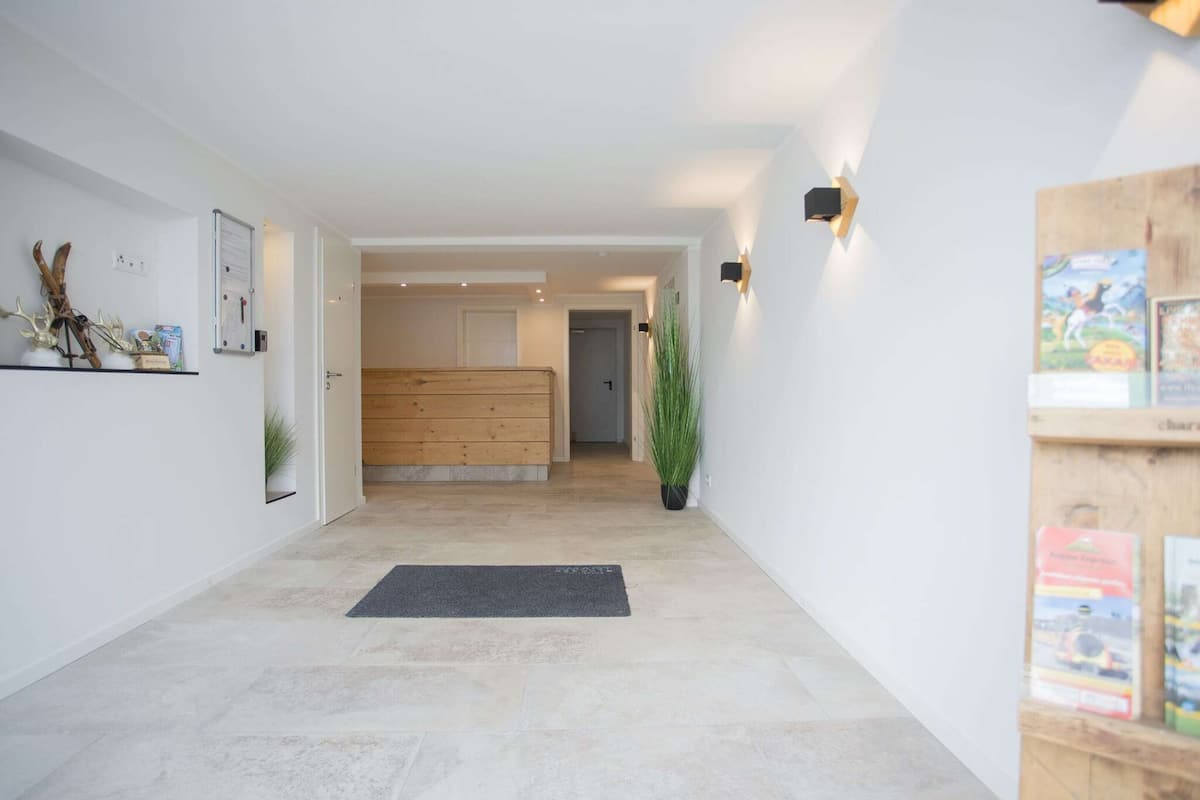 A hallway with a wooden bench, a black mat, and a potted plant.