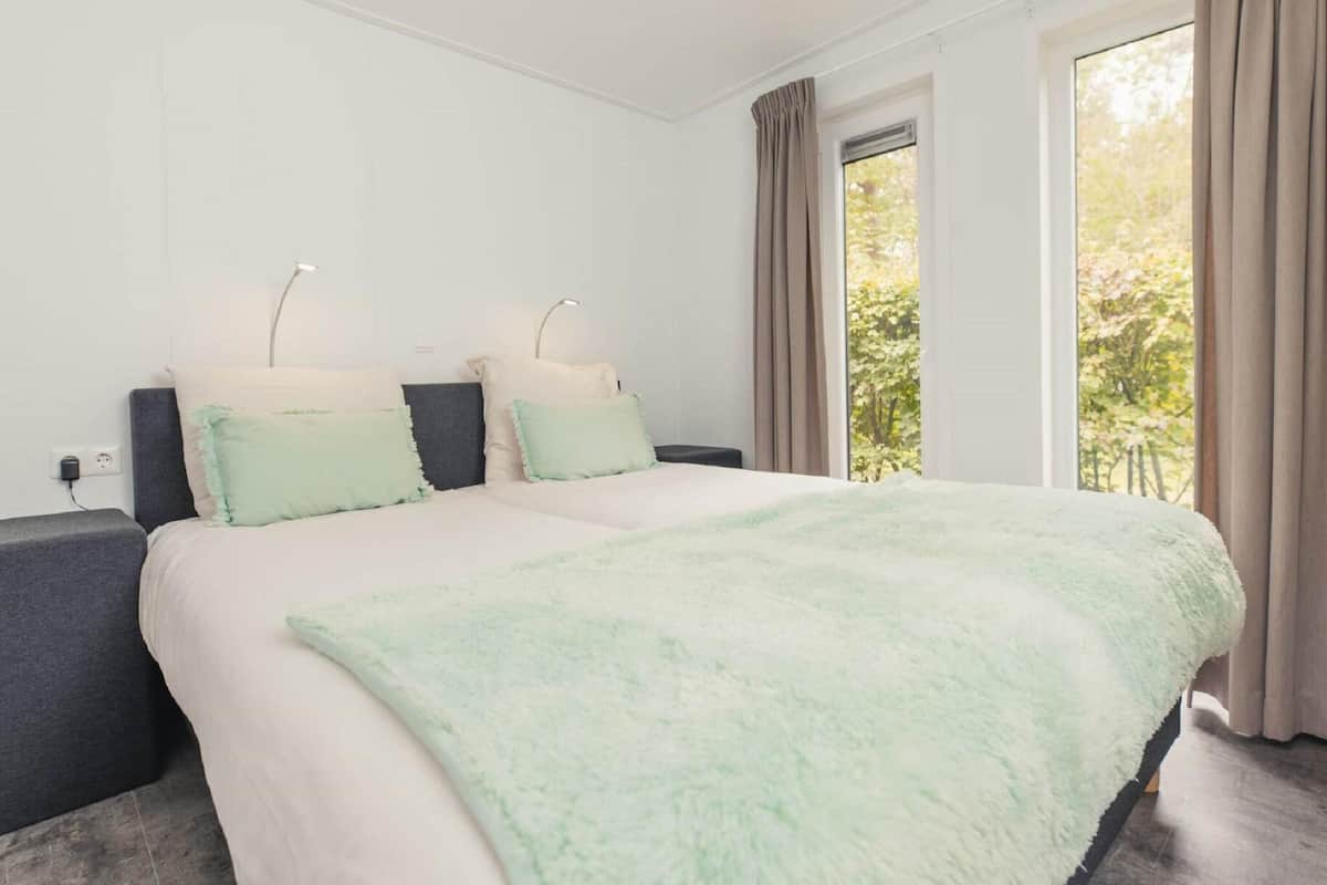 A modern bedroom with a large bed, two bedside tables, and a window with curtains.