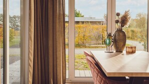 Una habitación con un amplio ventanal, una mesa de madera y un jarrón con plantas secas.