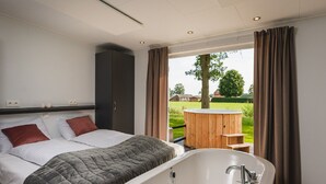 Un dormitorio con una cama grande, una bañera y vistas a un jacuzzi y jardín.