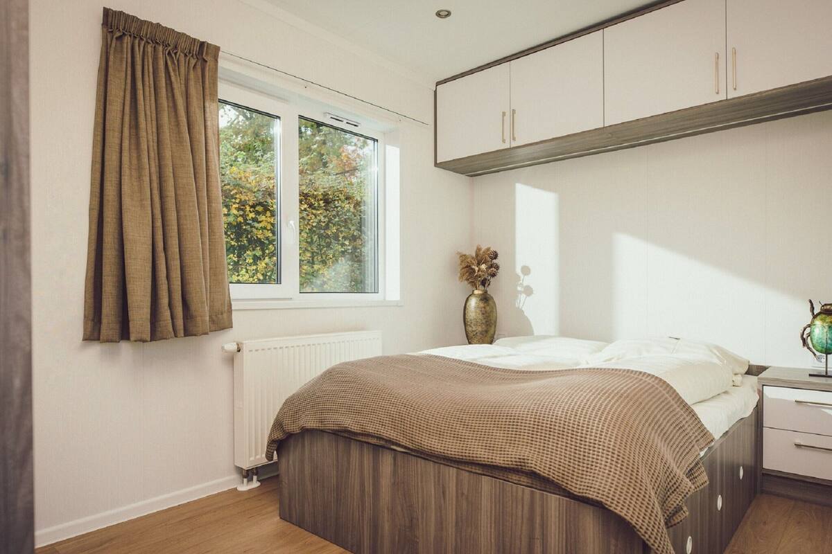 A bedroom with a bed, a nightstand, a dresser, a window with curtains, and a radiator.