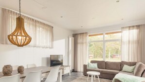 Una sala de estar moderna con comedor, un sofá, un televisor y un amplio ventanal con cortinas.