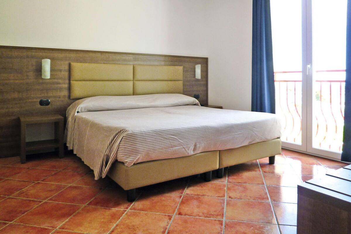 A hotel room with a bed, nightstand, and a view of a balcony.