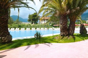A pool area with lounge chairs, palm trees, and a building in the background.