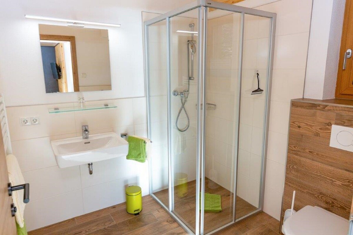 A bathroom with a glass shower enclosure, a sink, a mirror, and a wooden cabinet.