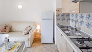 A compact kitchen with a refrigerator, stove, and sink. There's a small table with a lamp and a coffee maker. - Apartment in Loano With Garden (Loano)