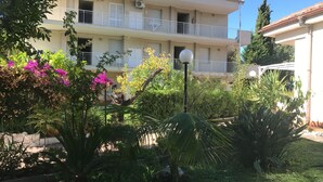 A multi-story building with balconies, surrounded by lush greenery and flowering plants. - Apartment in Loano With Garden (Loano)