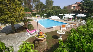 Una piscina con lettini e ombrelloni, circondata da vegetazione e un vialetto in pietra.