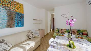 Ein modernes Wohnzimmer mit einem beigen Sofa, einem farbenfrohen Sofa, einem Esstisch mit floralem Tischlaufach und einem großen abstrakten Gemälde an der Wand.