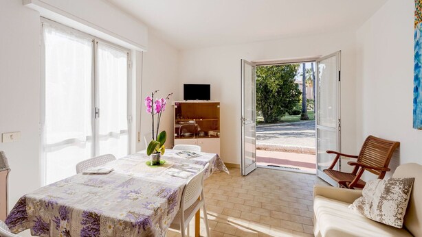 A bright living room with a dining table, a sofa, and a TV on a shelf. - Apartment in Loano With Garden (Loano)