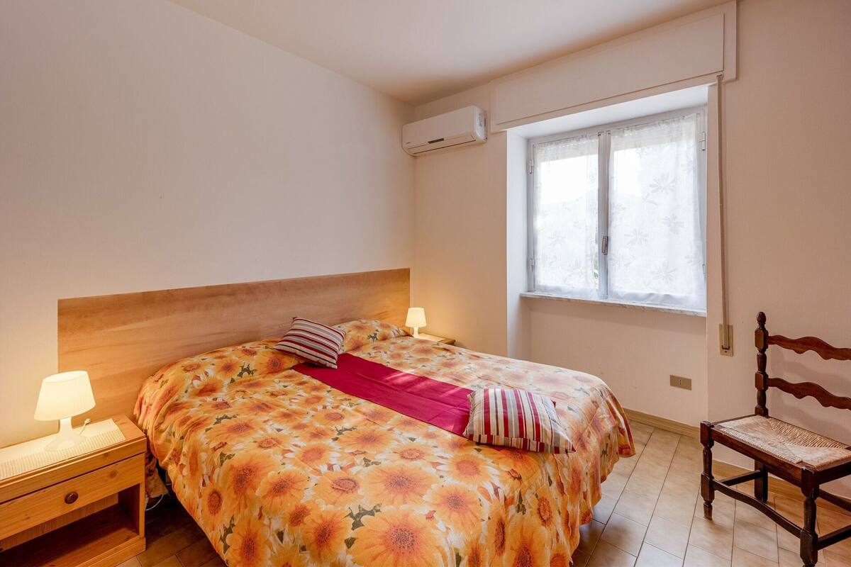 Un dormitorio con una cama, una mesita de noche, una silla, una ventana y un aire acondicionado.