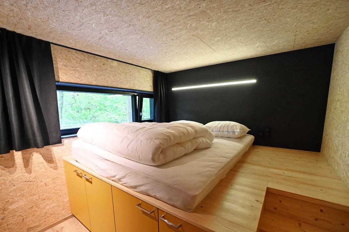 Une chambre à coucher de taille modeste, comprenant un lit, des armoires en bois, une fenêtre et un mur noir.