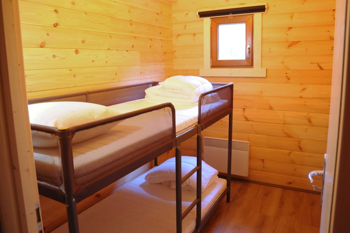 Une petite pièce en bois, aménagée comme une cabine, avec des lits superposés, une fenêtre et un radiateur.