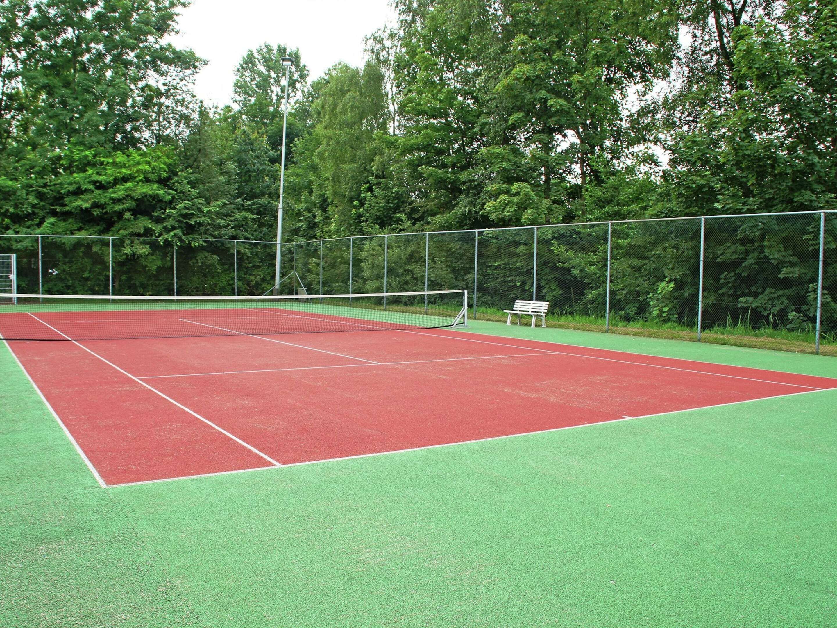 A tennis court with a net, green and red playing surfaces, and a bench.