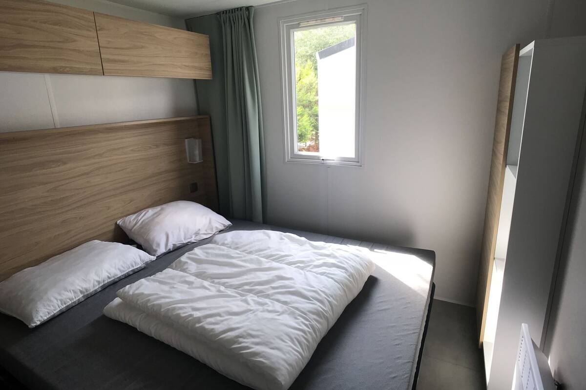 A single bed with a wooden headboard, a window with curtains, and a radiator on the wall.