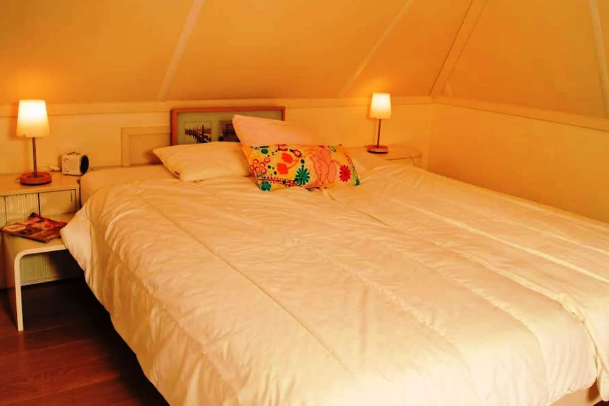 A single bed in a room with a sloped ceiling, two bedside tables with lamps, and a small shelf with books.