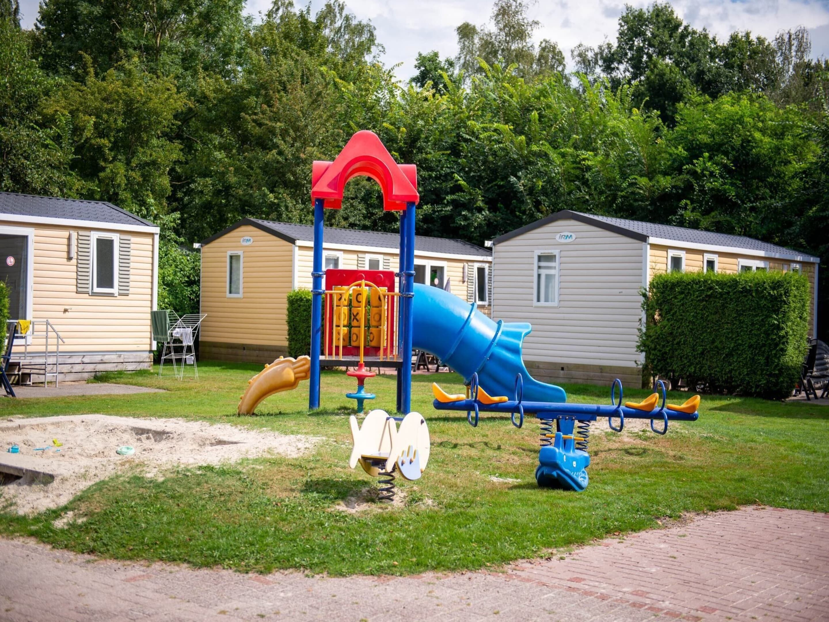 A playground with a slide and swings, surrounded by mobile homes.