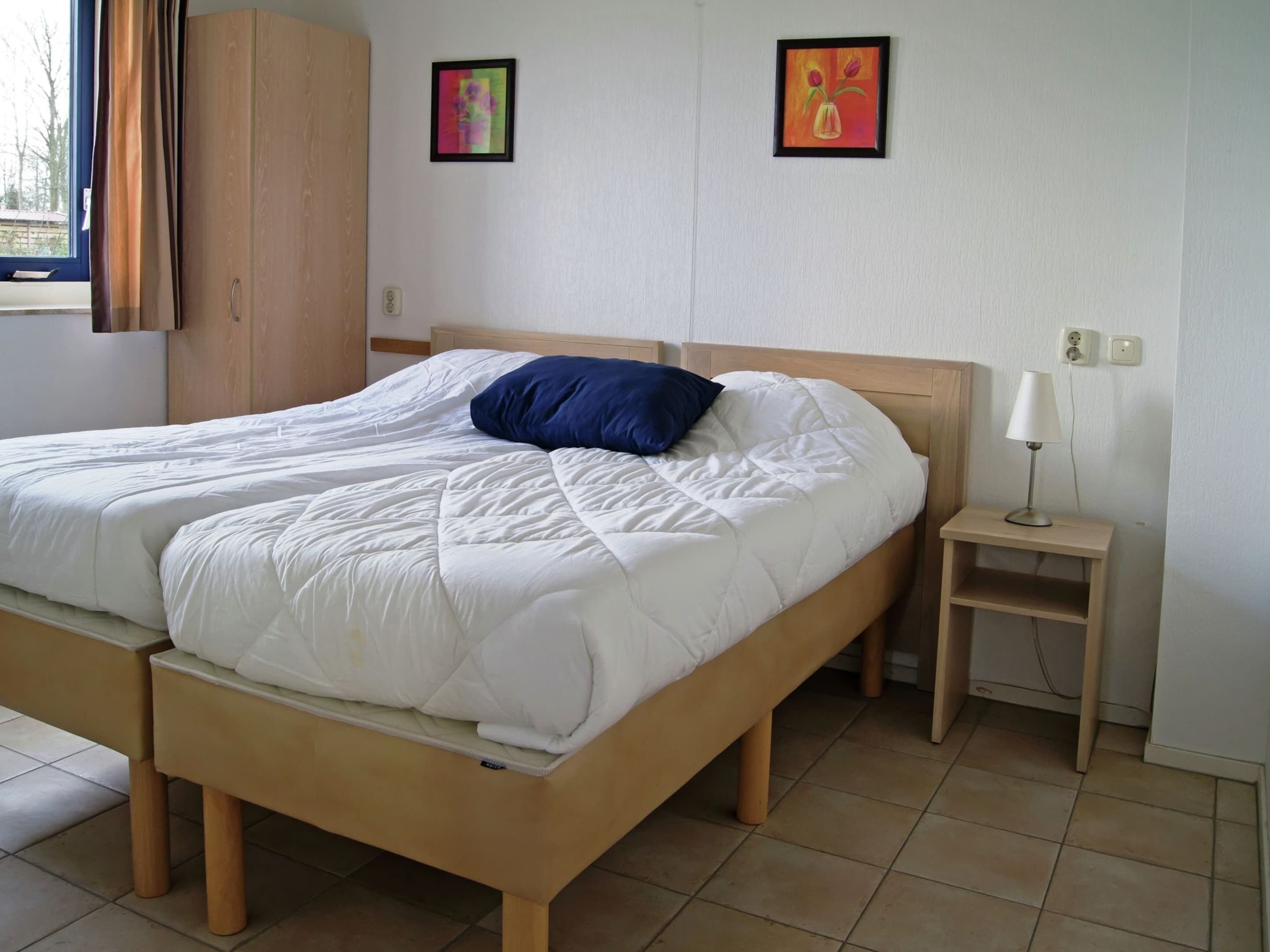 A double bed with a blue pillow, a bedside table with a lamp, and two framed pictures on the wall.