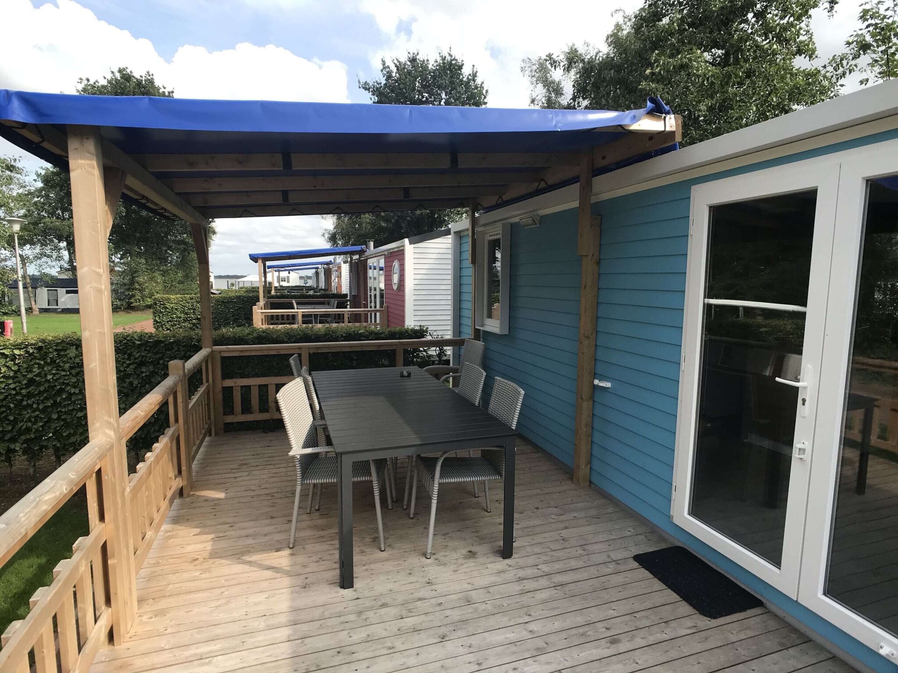 Une terrasse extérieure couverte, dotée d’une table et de chaises, d’une rambarde en bois et d’une porte-fenêtre coulissante.