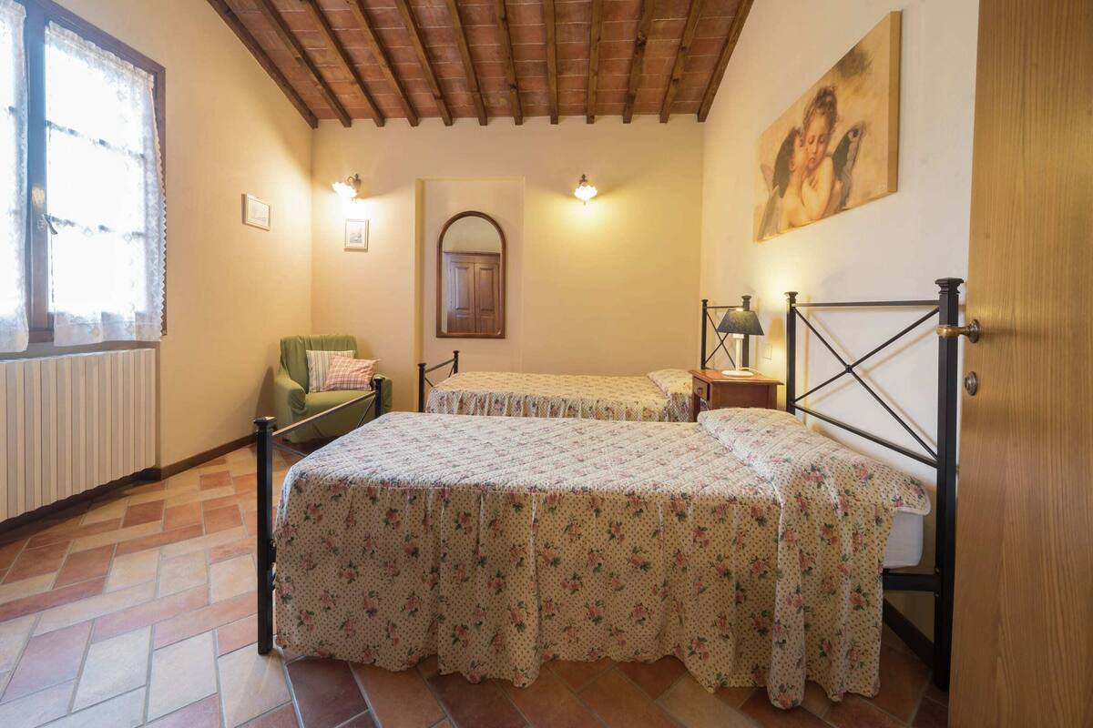 A room with two single beds, a chair, a radiator, a wooden ceiling, and a painting on the wall.