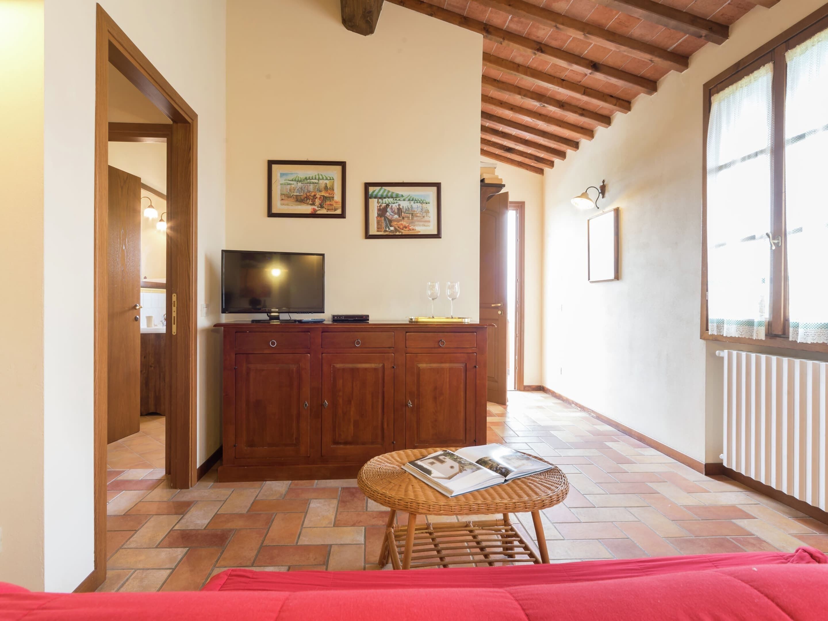 A cozy room with a wooden cabinet, a television, and a wicker table with magazines.