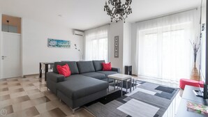 Ein modernes Wohnzimmer mit einem grauen Ecksofa, einem kleinen weißen Tisch und einer Kronleuchter.