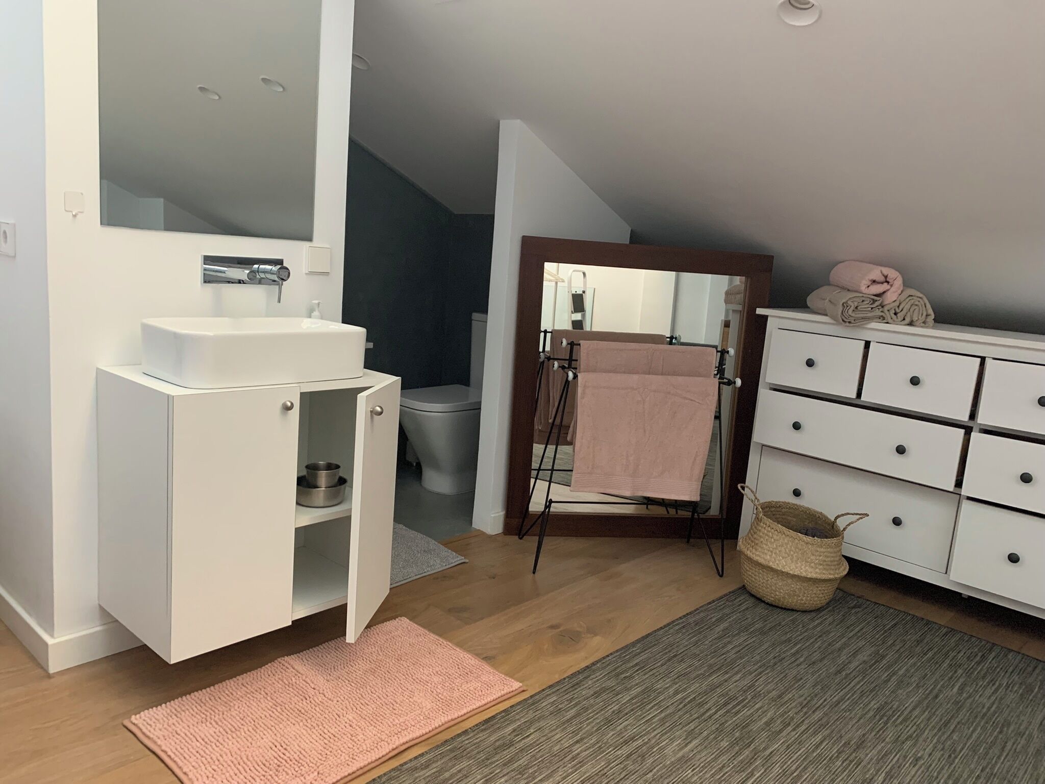Un baño moderno con tocador blanco, espejo, lavamanos, inodoro y toallero.