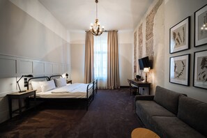 A hotel room with a bed, a desk, a sofa, a chandelier, and framed botanical prints on the wall. - Arche Hotel Klasztor Wrocław (Wroclaw)