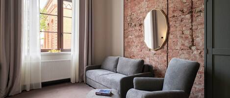 A room with a grey sofa, an ottoman, a large mirror, and a brick wall.