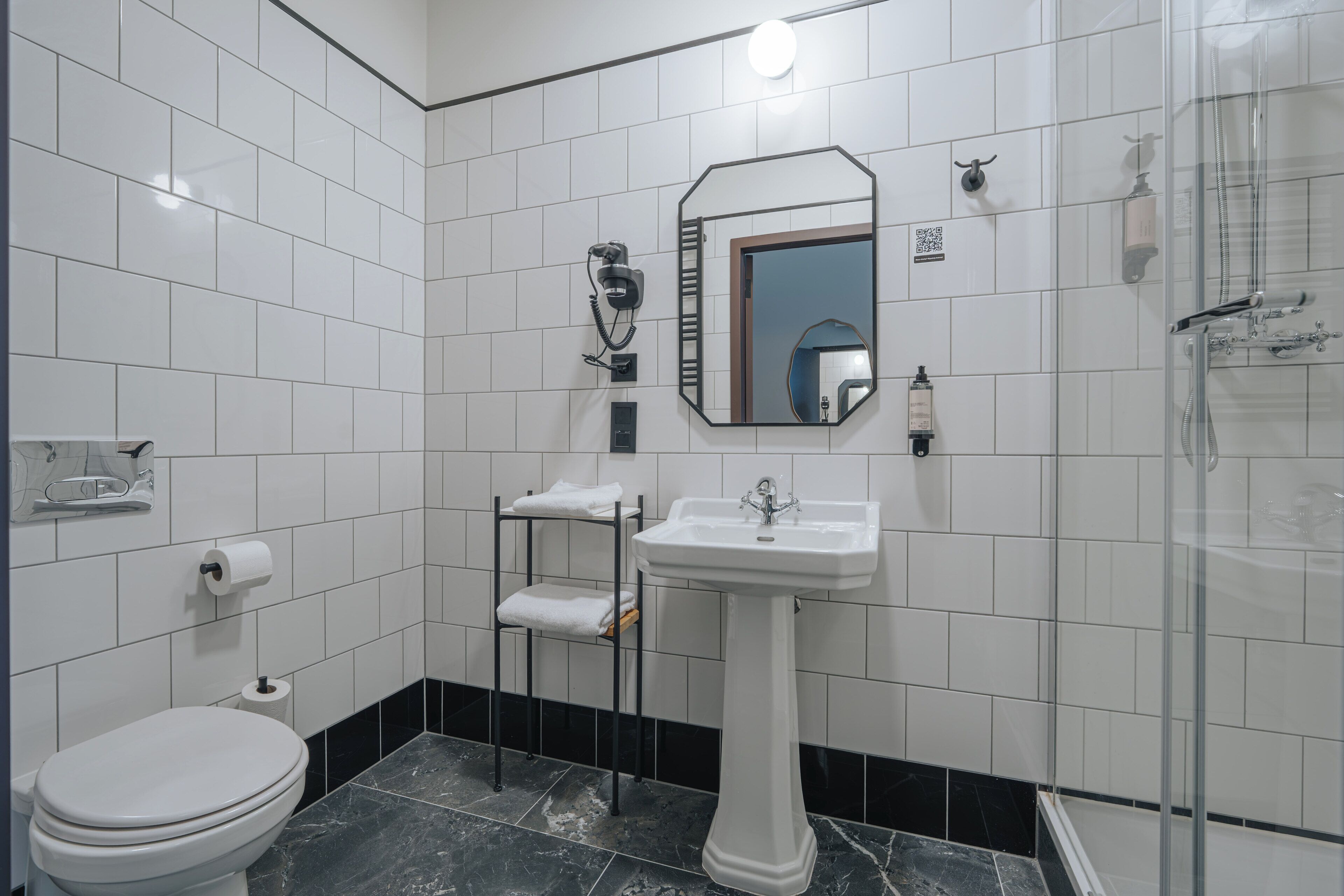 Ein Badezimmer mit weißer Toilette, einem Standwaschbecken, einem Spiegel, einem Handtuchhalter und einer Duschkabine.