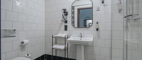 Een badkamer met een wit toilet, een wastafel op voet, een spiegel, een handdoekrek en een douchegedeelte.