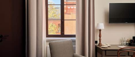 A room with a window, a chair, a desk, a lamp, and a flat-screen TV.