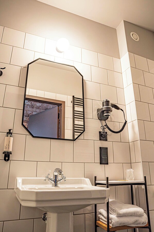Un baño con lavamanos blanco, un espejo, un perchero para toallas y un teléfono instalado en la pared.
