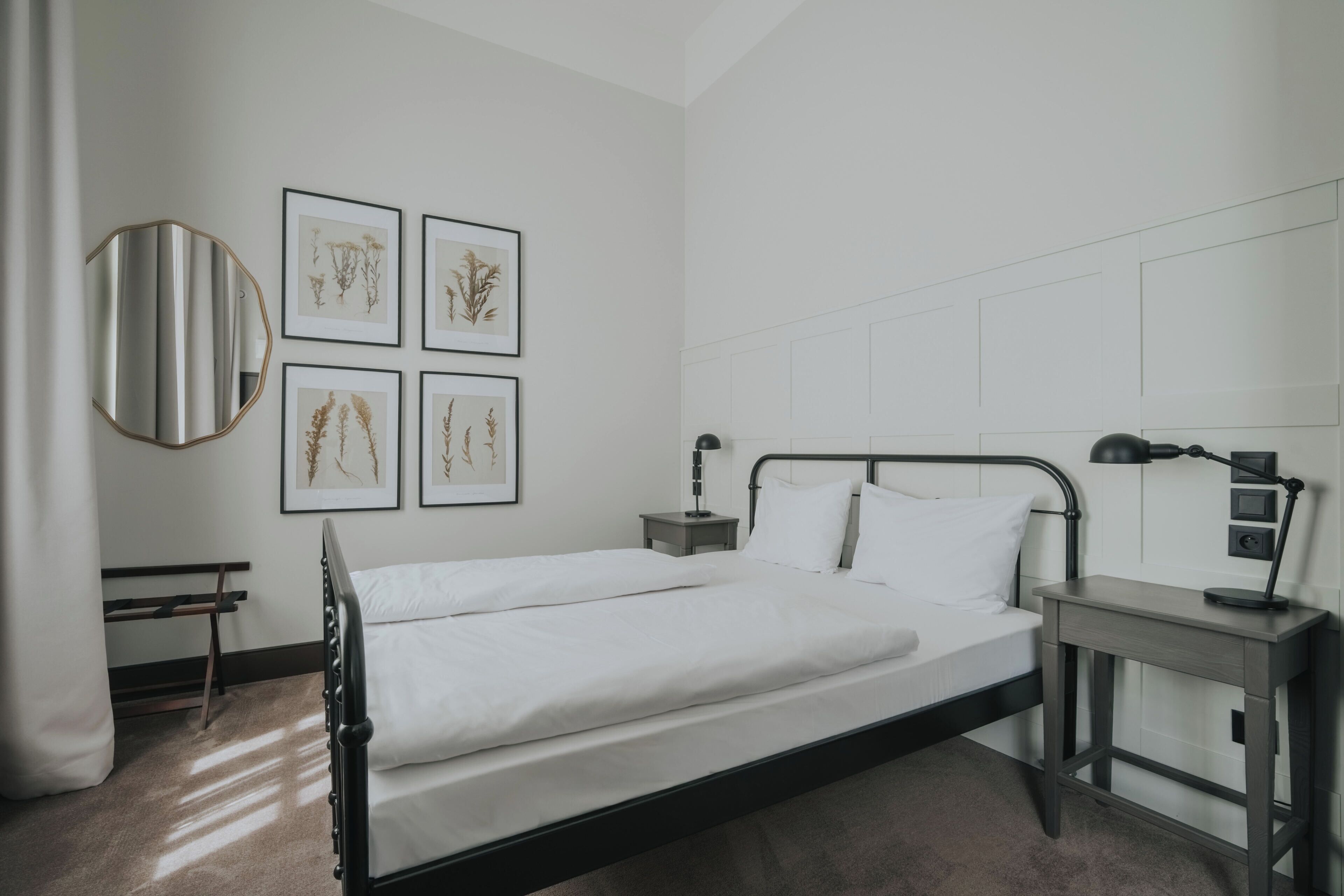Une chambre à coucher moderne avec un lit double, des tables de chevet, un bureau et des reproductions botaniques encadrées accrochées au mur.