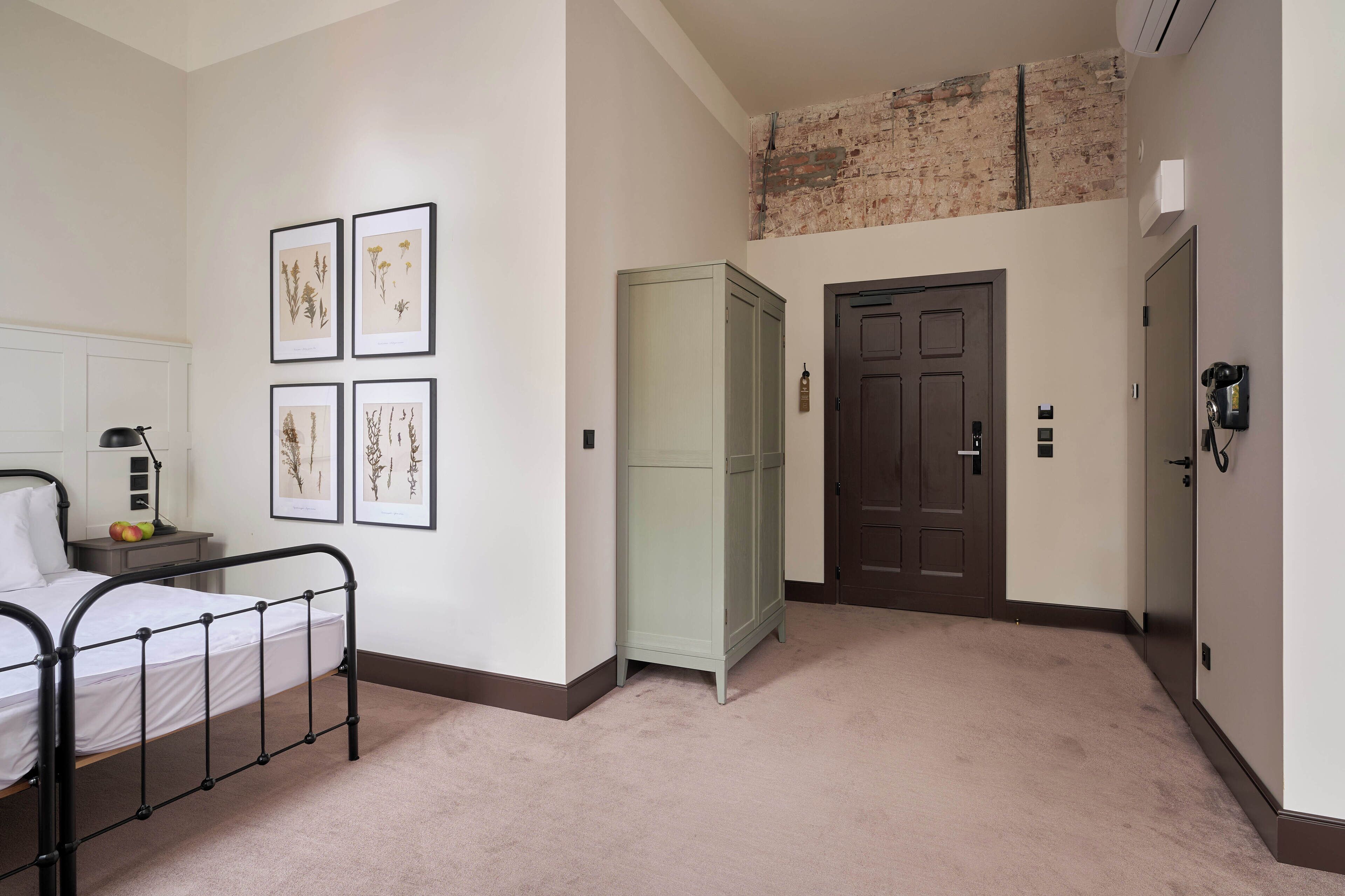 Una camera da letto con un letto, un comodino, stampe botaniche incorniciate, un armadio e una porta.