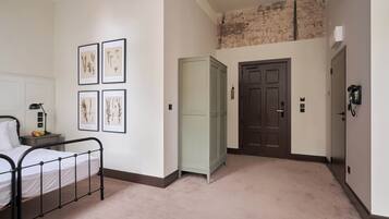 A bedroom with a bed, a nightstand, framed botanical prints, a wardrobe, and a door.