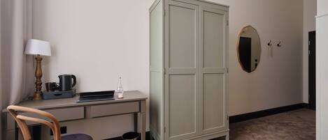 A small room with a desk, chair, wardrobe, and a mirror.